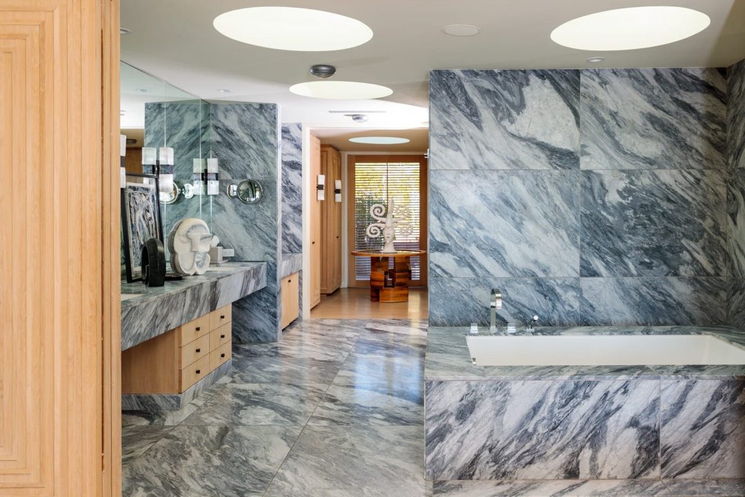 Large bathroom with marble floors and wall, and sink with large mirror