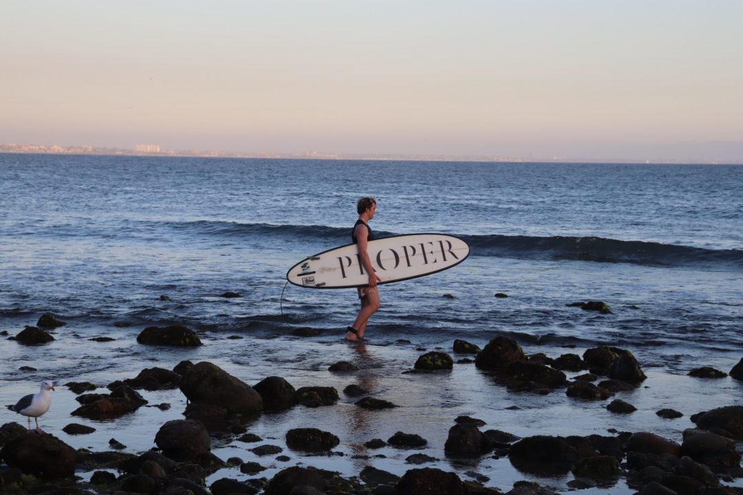 Guy with Proper branded surfboard standing on beach