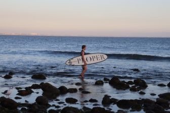 Guy with Proper branded surfboard standing on beach