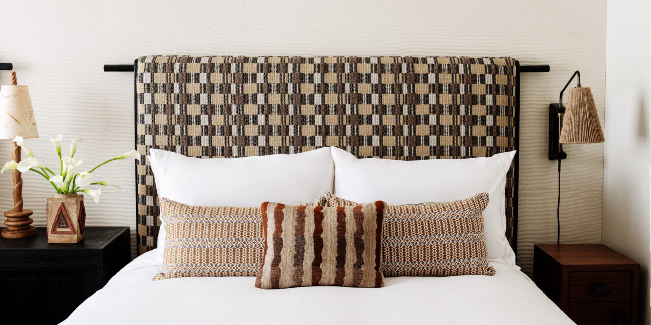 Stylish guest room bed with patterned headboard, layered pillows, and modern bedside lighting