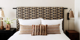 Stylish guest room bed with patterned headboard, layered pillows, and modern bedside lighting