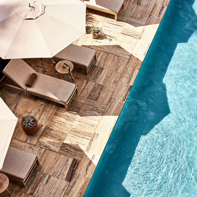 Top-down view of a poolside deck with lounge chairs, umbrellas, and clear blue water
