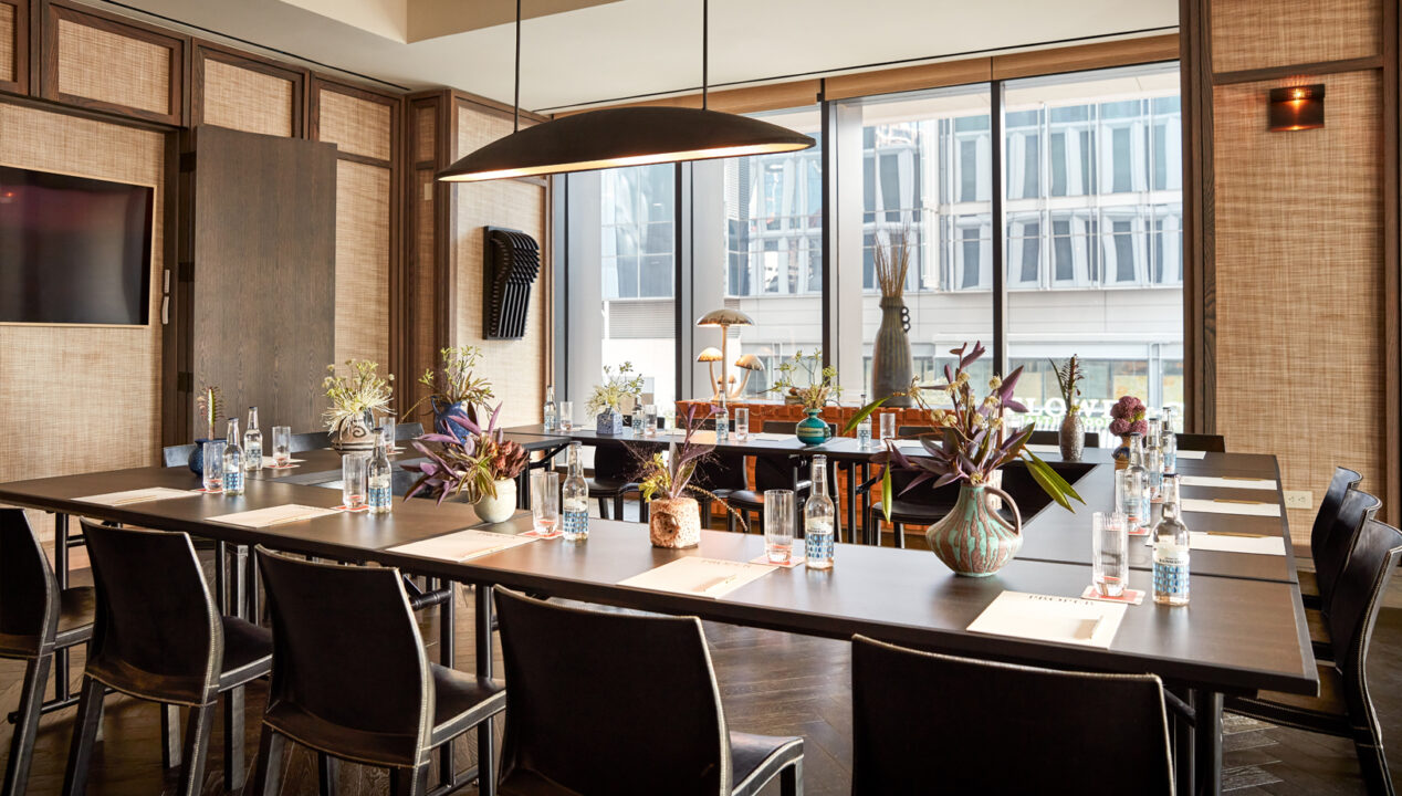 Modern meeting room setup with arranged tables, chairs, floral decor, and natural light from large windows