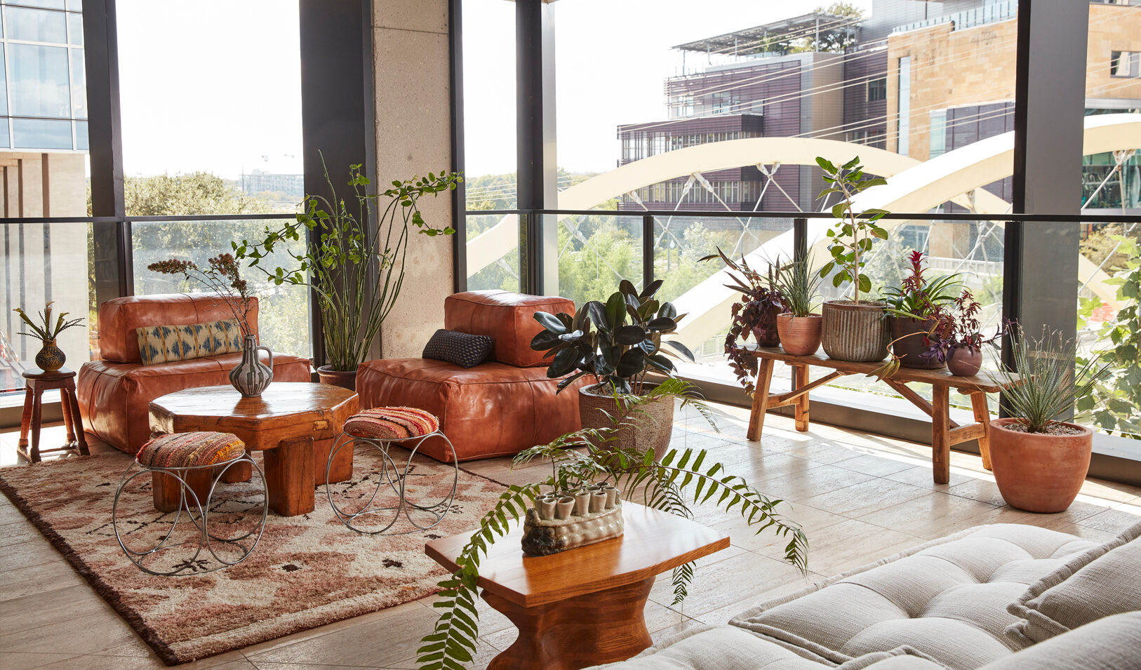 Bright lounge with leather seating, indoor plants, and floor-to-ceiling windows with city views