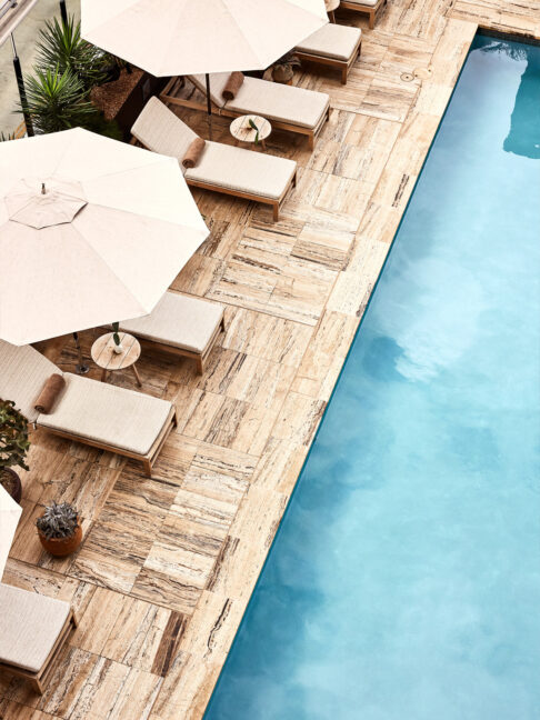 Top-down view of a poolside deck with lounge chairs, umbrellas, and clear blue water