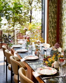 Intimate dining setup with floral arrangements, patterned plates, and elegant tableware in a sunlit space
