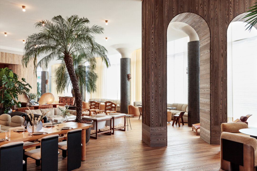 Elegant dining and lounge space with palm trees, wood accents, and contemporary seating design