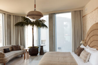 Bright modern hotel suite with curved sofa, king bed, floor to ceiling windows, and indoor palm tree