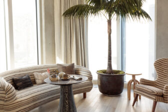 Sunlit hotel suite lounge with curved striped sofa, indoor palm tree, and cozy seating area by floor to ceiling windows