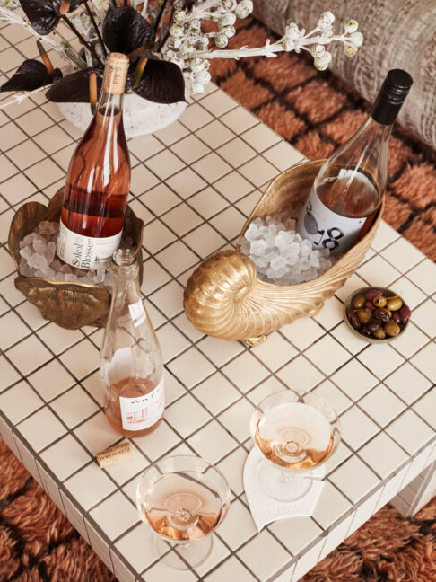 Rosé wine bottles chilling in ice buckets on a tiled table with glasses and olives nearby