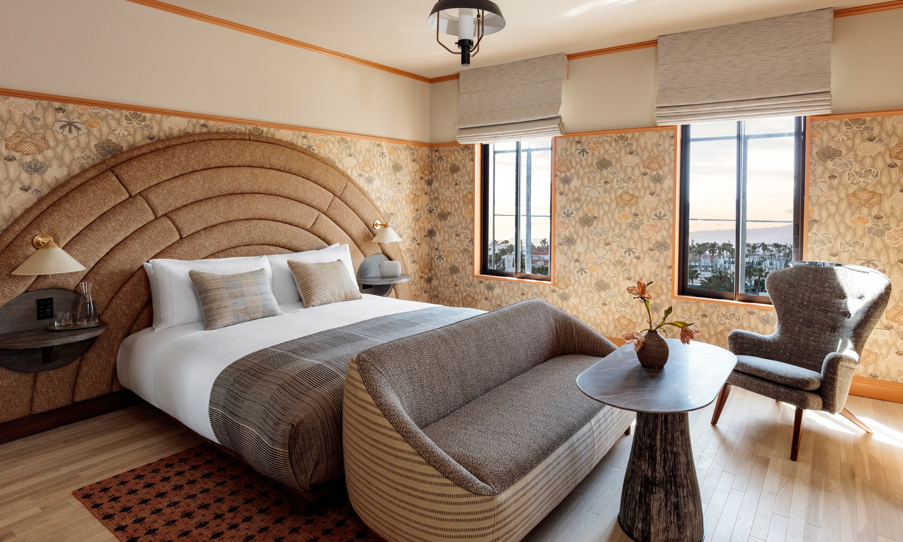 Elegant hotel suite with king bed, curved headboard, lounge seating, and city view windows