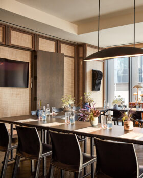 Modern meeting room setup with arranged tables, chairs, floral decor, and natural light from large windows