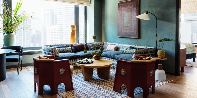 Living room area with sectional sofa, chairs, coffee table, and large window with view of Downtown LA buildings
