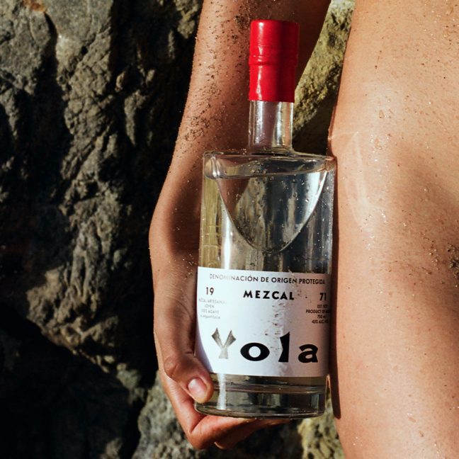 Hand holding a mezcal bottle on a sandy beach