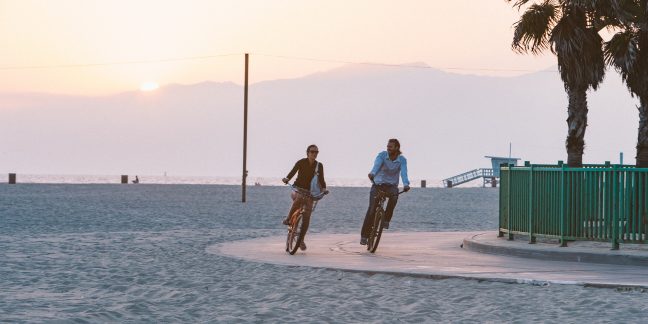 Couple riding bikes on wide sidewalk next to beach