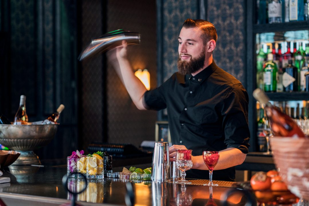 Bartender preparing cocktails at upscale rooftop bar with illuminated back bar display