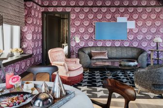 Luxury hotel suite with patterned wallpaper, designer lounge seating, and in room dining setup