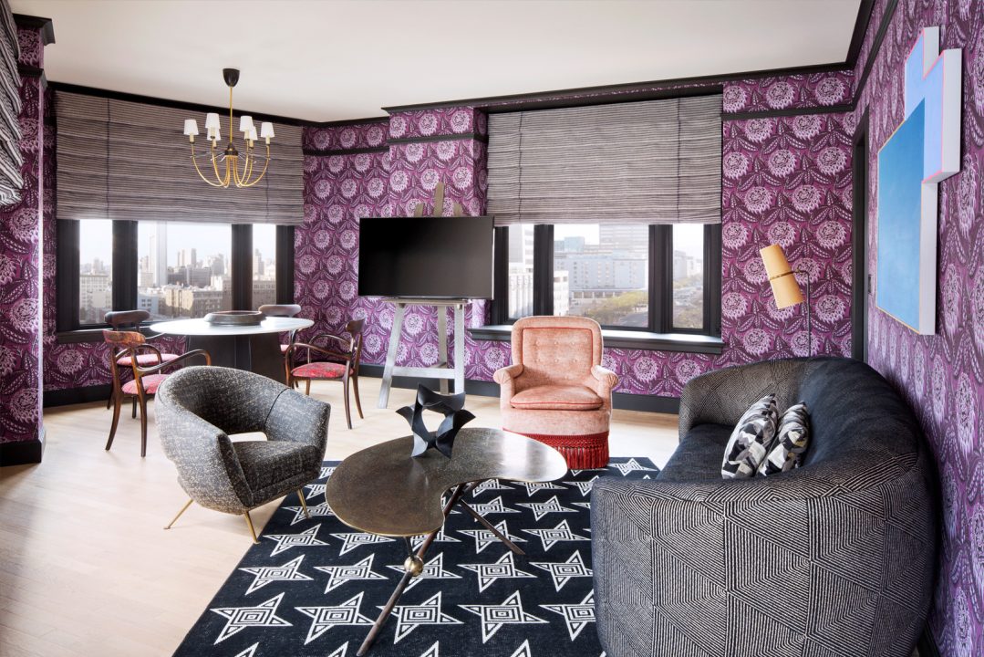 Stylish hotel suite with patterned wallpaper, lounge seating, and city view windows