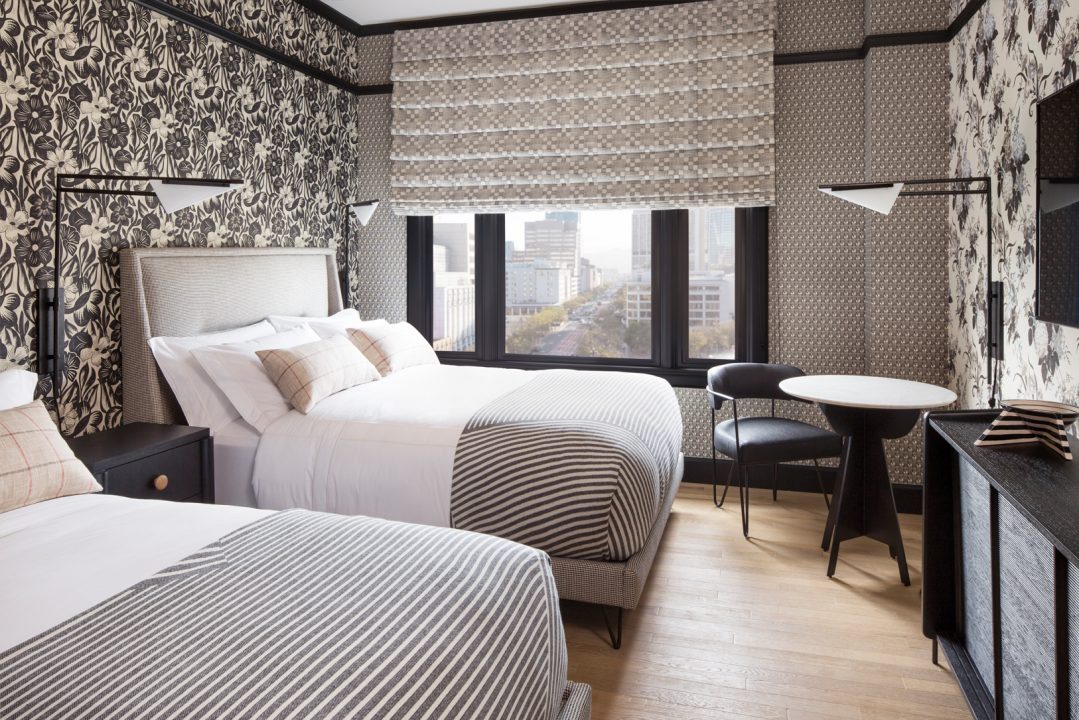 Luxury hotel guest room with patterned walls, double beds, and city view window