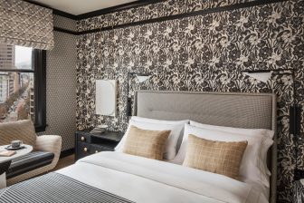 hotel bed with pillows, walls with patterns, sofa, and window with city view