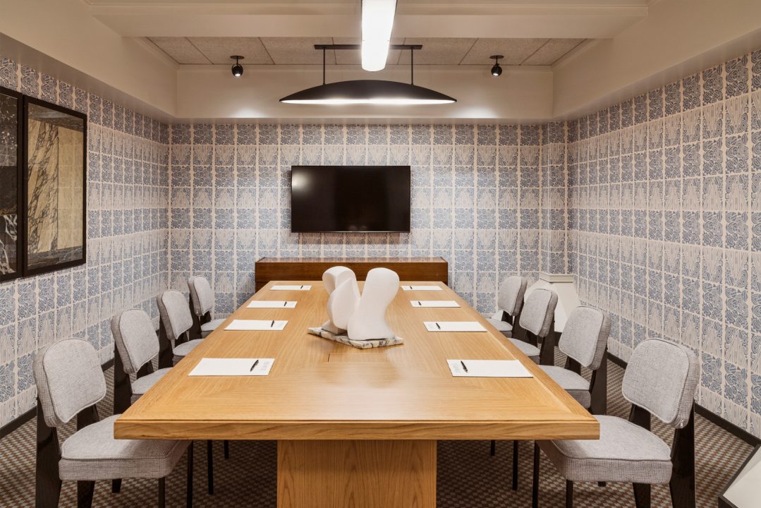 Private hotel boardroom with conference table, patterned walls, and mounted presentation screen