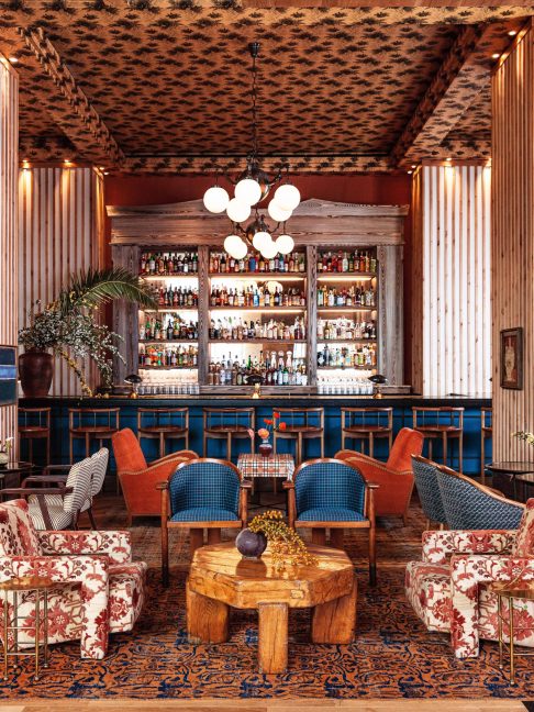 Stylish hotel lounge with patterned seating, wood accents, and a fully stocked bar at the center