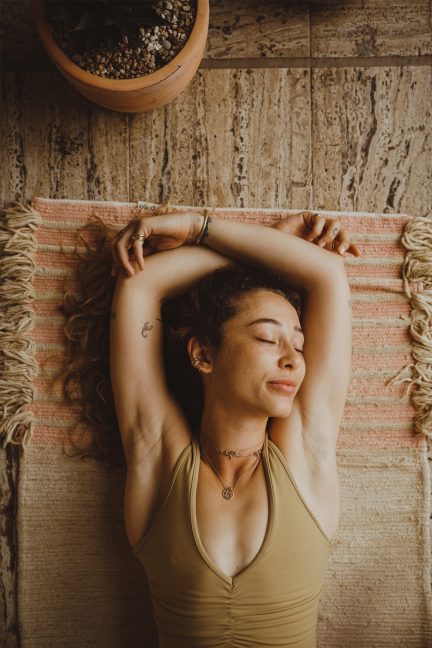 Woman lying on a yoga mat with eyes closed, relaxing in a calm indoor setting