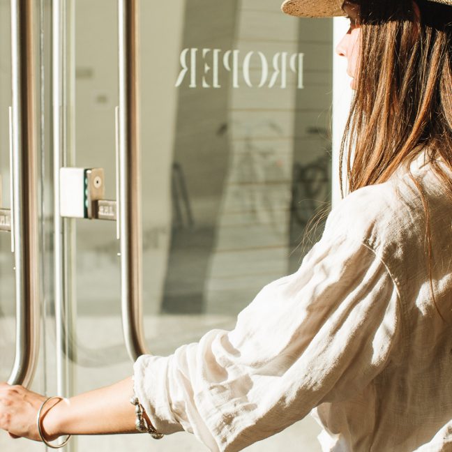 Woman wearing a straw hat opening a glass door at a boutique entrance