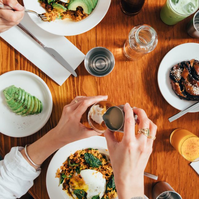 Overhead view of brunch dishes with eggs, avocado, and drinks on a wooden table