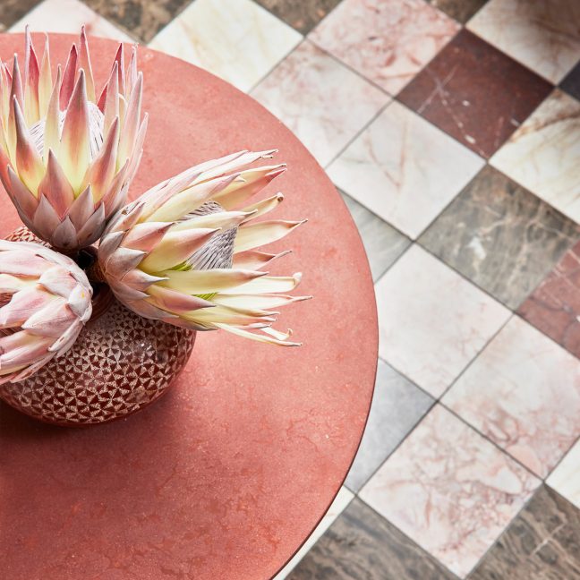Pink protea flowers in a textured vase on a round coral table