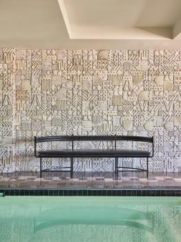 Indoor pool lounge with sculptural decor, patterned tile walls, and modern seating