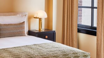 Cozy bedroom corner with plush bedding, brass table lamp, and natural light by the window