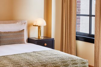 Cozy bedroom corner with plush bedding, brass table lamp, and natural light by the window