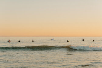 The image appears to depict a serene ocean scene at sunset with a group of people sitting on surfboards, waiting for waves.
