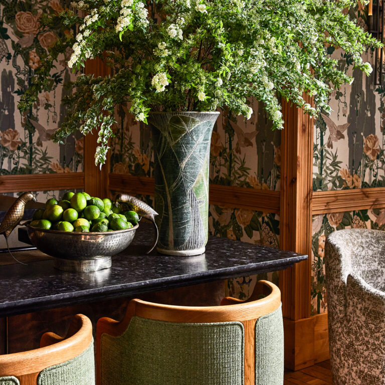 Decorative interior vignette with a vase of flowers and a bowl of limes on a marble counter against patterned wallpaper
