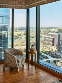 Corner seating area with armchair, side table, and floor-to-ceiling city view windows