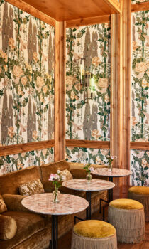 Cozy lounge with upholstered seating, marble tables, and small floral arrangements in soft natural light