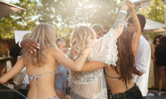 People enjoy a daytime garden party, holding hands as they revel together.