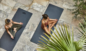 Two women practice yoga on mats spread out across the floor.