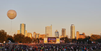 Large outdoor music festival with city skyline backdrop