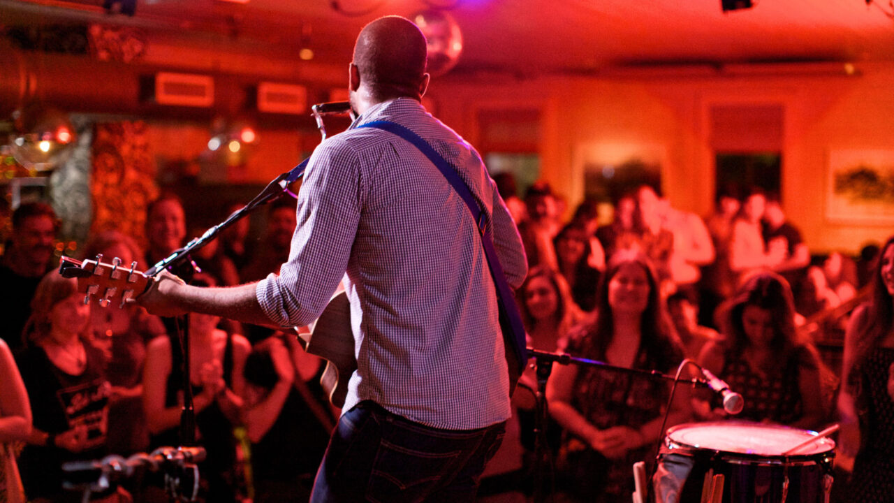 Live music performance with guitarist playing to a crowd in a vibrant indoor venue