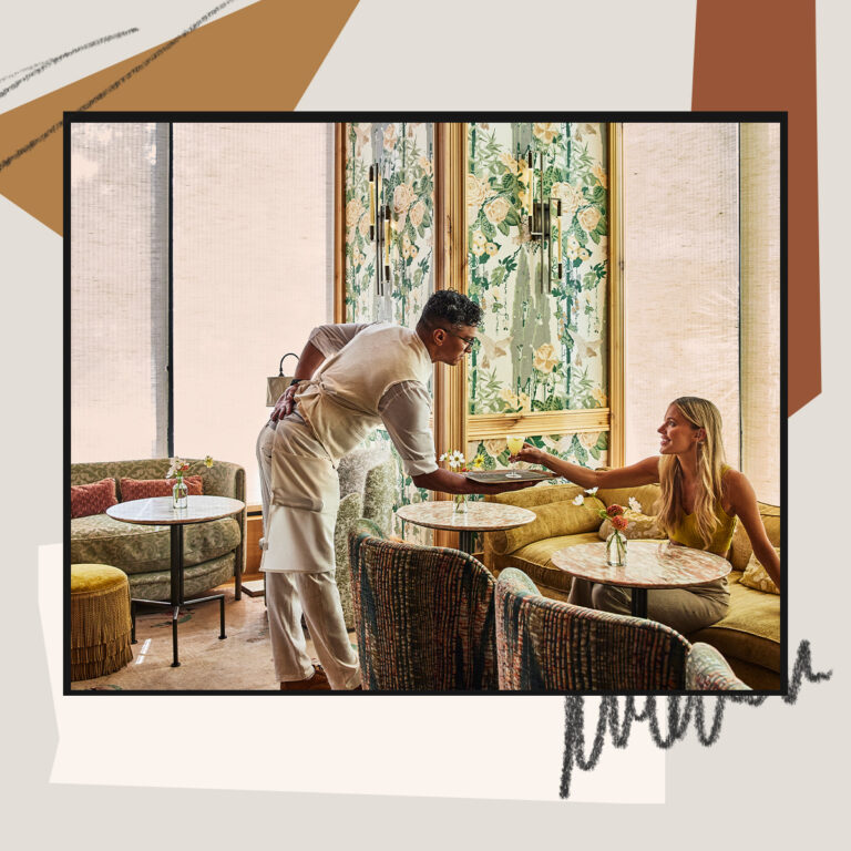 Server handing a drink to a guest seated in a stylish lounge with floral decor