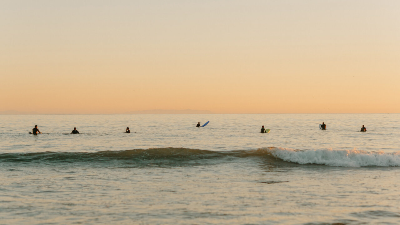 Surfers waiting on calm ocean waves during sunset along scenic coastal shoreline