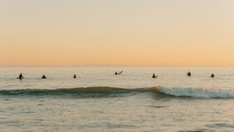 Surfers waiting on calm ocean waves during sunset along scenic coastal shoreline