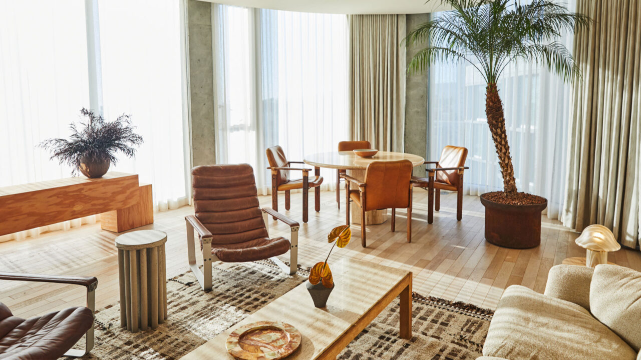 Sunlit hotel suite with leather chairs, dining table, and indoor palm
