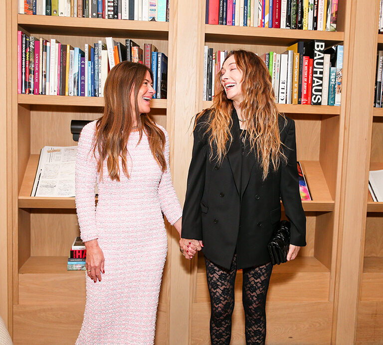 Two women smiling together in front of a bookshelf
