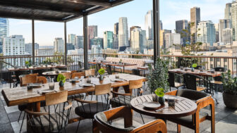 A rooftop dining area offers tables, chairs, and a stunning view of city skyscrapers.