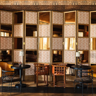 Cozy lounge nook with patterned screens, small tables, and stylish seating in a warm, vintage-inspired setting
