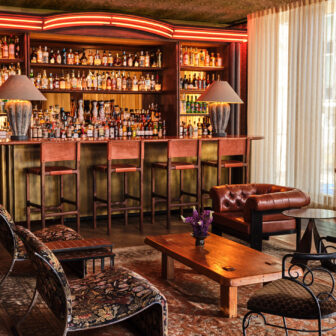 Warm, stylish lounge with leather seating, a piano, and a fully stocked bar in a vintage-inspired setting