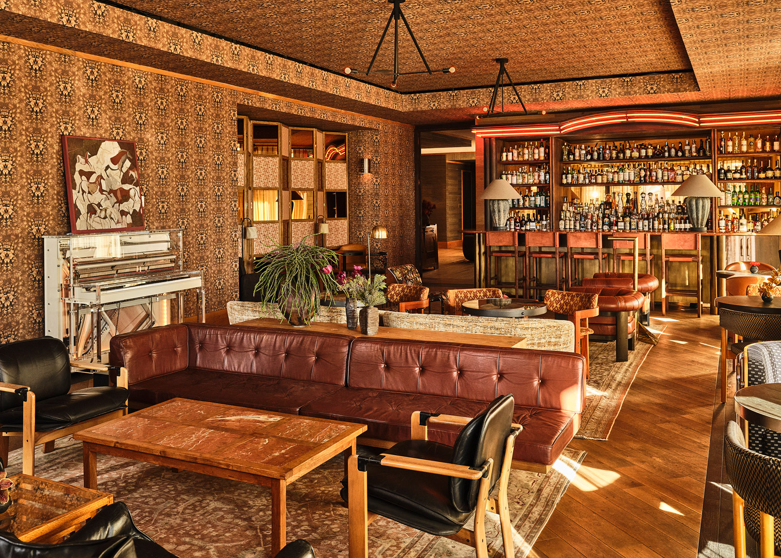 Warm, stylish lounge with leather seating, a piano, and a fully stocked bar in a vintage-inspired setting